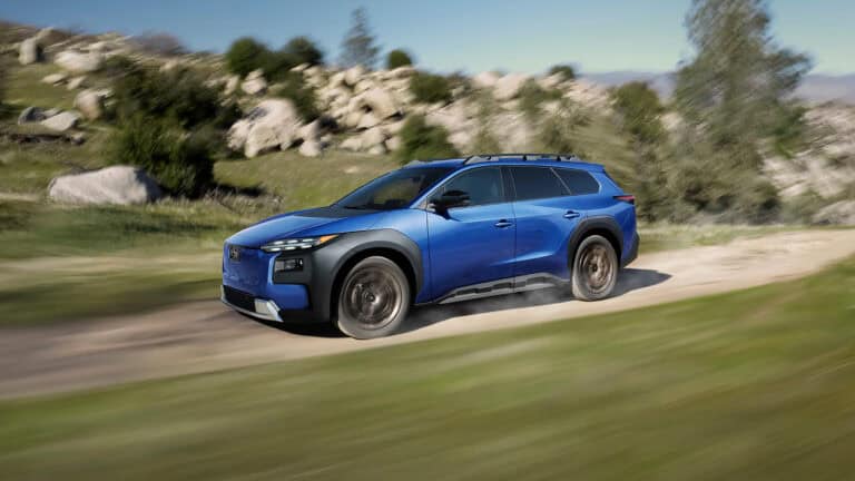 Blue 2026 Subaru Trailseeker EV driving on a dirt road, showcasing its dual-motor AWD, off-road traction, and raised ground clearance.