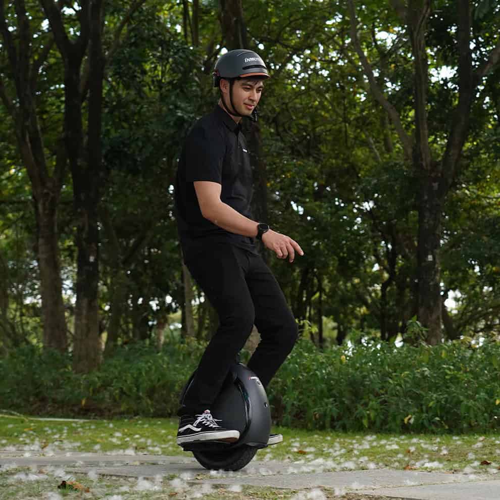 Rider cruising on an Inmotion V6 electric unicycle along a leafy path in the park, maneuvering smoothly over uneven ground under tree cover.