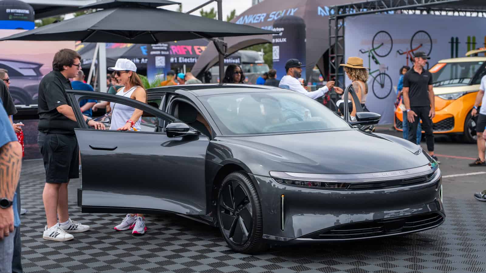 Lucid Air electric sedan with doors open at Electrify Expo Phoenix, as attendees interact with the vehicle and staff