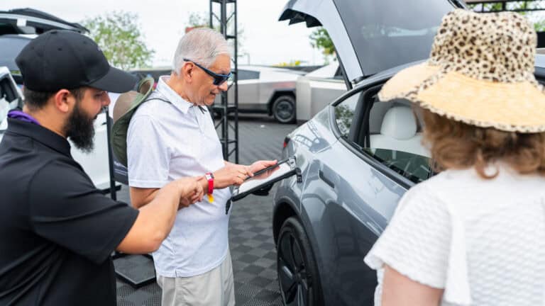 Attendee signing up for a Tesla Model Y test drive using a tablet at Electrify Expo Phoenix, with staff assistance and the vehicle in view.