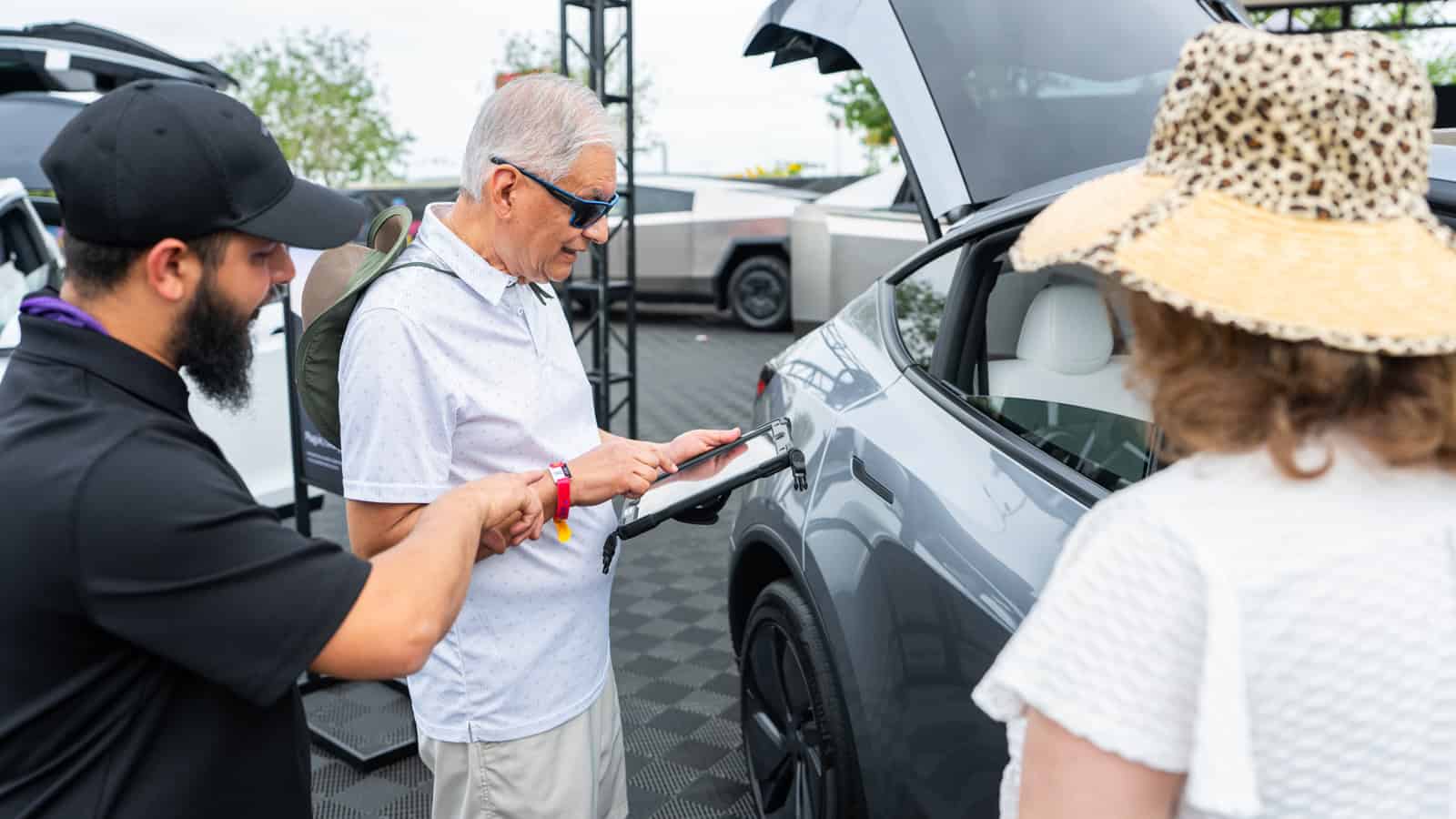 Attendee signing up for a Tesla Model Y test drive using a tablet at Electrify Expo Phoenix, with staff assistance and the vehicle in view.