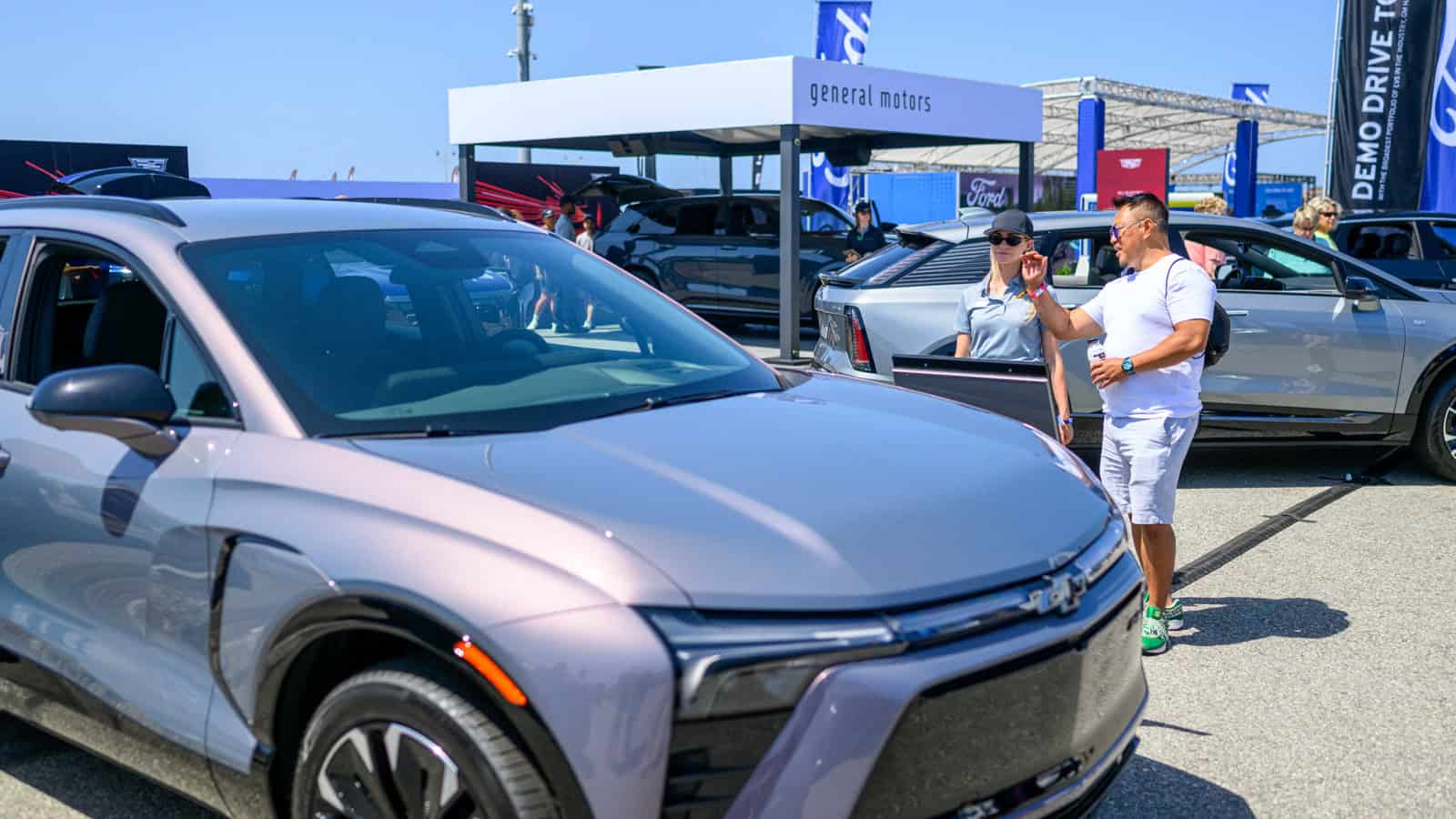 A man speaks with a GM rep next to Chevrolet, Cadillac, and GMC electric vehicles at Electrify Expo, highlighting LFP and LMR battery tech in action.
