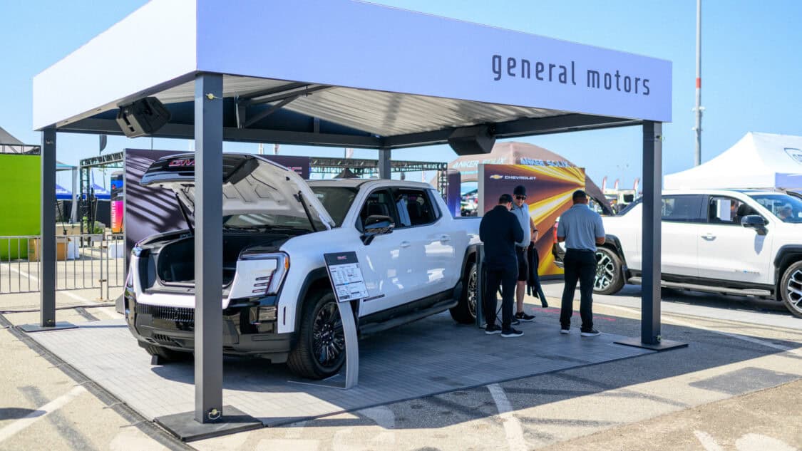 GMC Sierra electric trucks on display under a branded General Motors canopy as attendees learn about LFP and LMR battery technology at Electrify Expo.