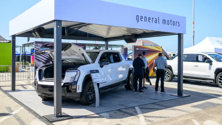 GMC Sierra electric trucks on display under a branded General Motors canopy as attendees learn about LFP and LMR battery technology at Electrify Expo.