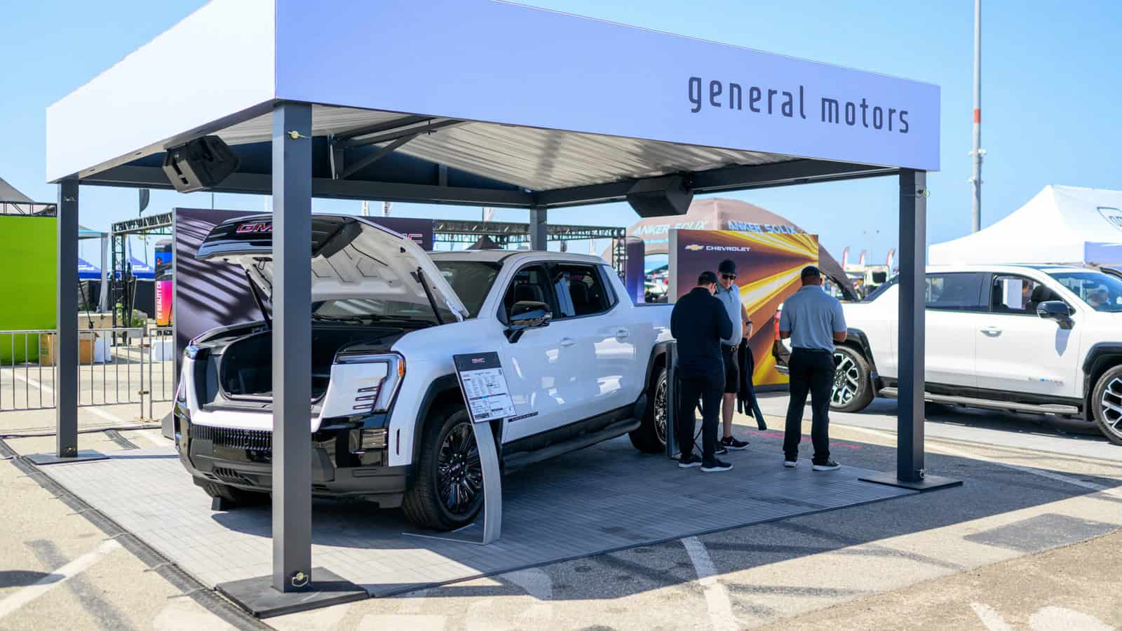 GMC Sierra electric trucks on display under a branded General Motors canopy as attendees learn about LFP and LMR battery technology at Electrify Expo.