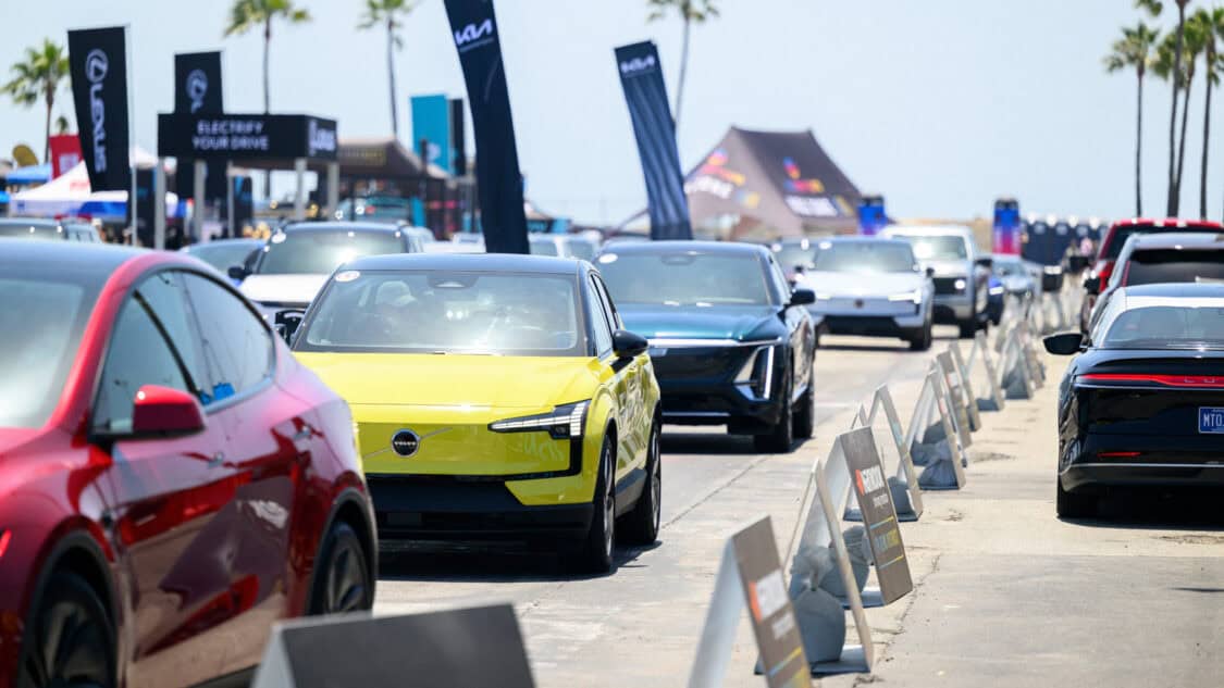 A Tesla Model 3 and Volvo EX30 lead a line of electric vehicles, including models from Cadillac, Lucid, Polestar, and Ford, during a test drive event at Electrify Expo.