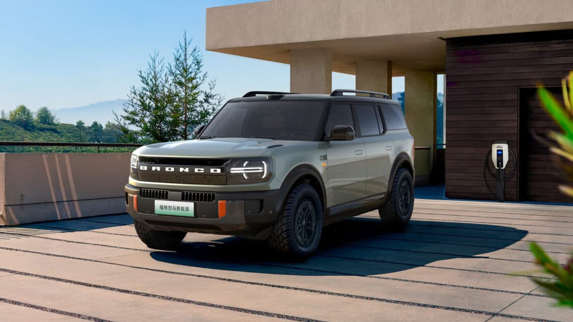 Ford Bronco New Energy electric SUV parked at a modern home with a Ford wall charger, highlighting its EV identity and residential charging setup.