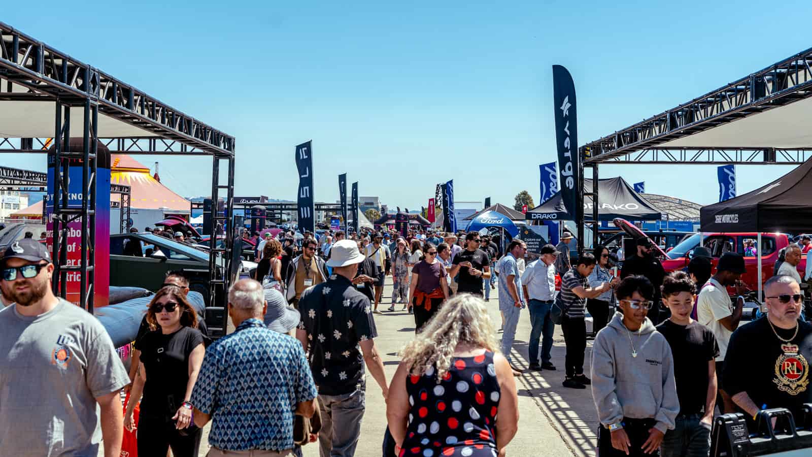 Crowds walk through Electrify Expo San Francisco lined with banners and dealer booths, highlighting the rush to secure federal tax credits before deadlines.