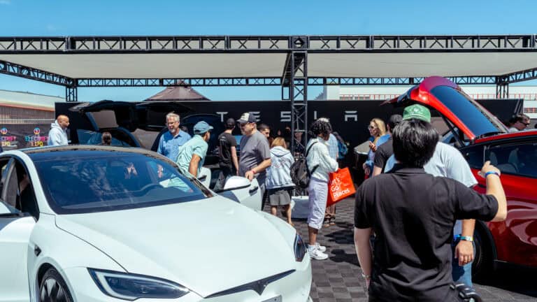 Visitors gather at a Tesla display during Electrify Expo, exploring EVs as buyers rush to secure federal tax credits before deadlines.