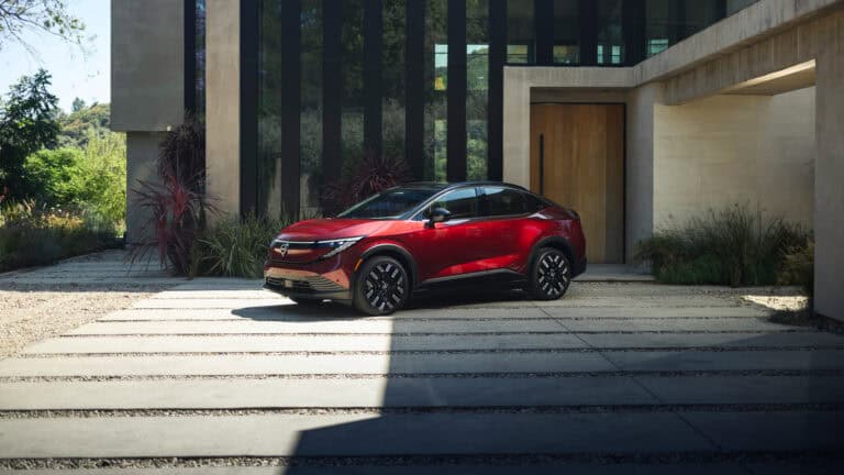 A red 2026 Nissan Leaf parked outside a modern home, highlighting its updated design as Nissan launches the new model under $30,000.