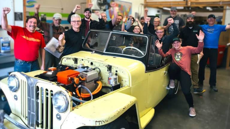 Group of Fuel2Electric and Switch Vehicles trainees celebrating around a classic car converted to electric during hands-on EV training.