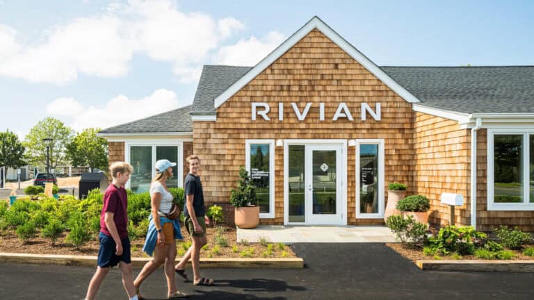 A family walks past Rivian’s cedar-shingled charging outpost in Southampton, blending Hamptons charm with all-day EV access and coastal comfort.