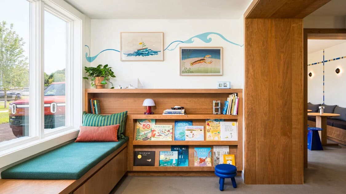 A cozy kids’ reading nook inside Rivian’s Southampton charging outpost, with ocean-themed art, books, and a Rivian R1T visible outside the window.