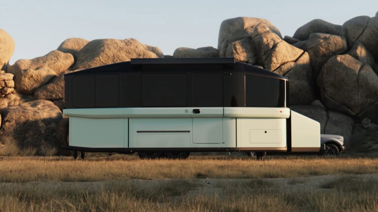 Lightship AE.1 Atmos ShadeMoss exterior in CampMode, parked in a rocky desert setting with panoramic windows and raised roofline.