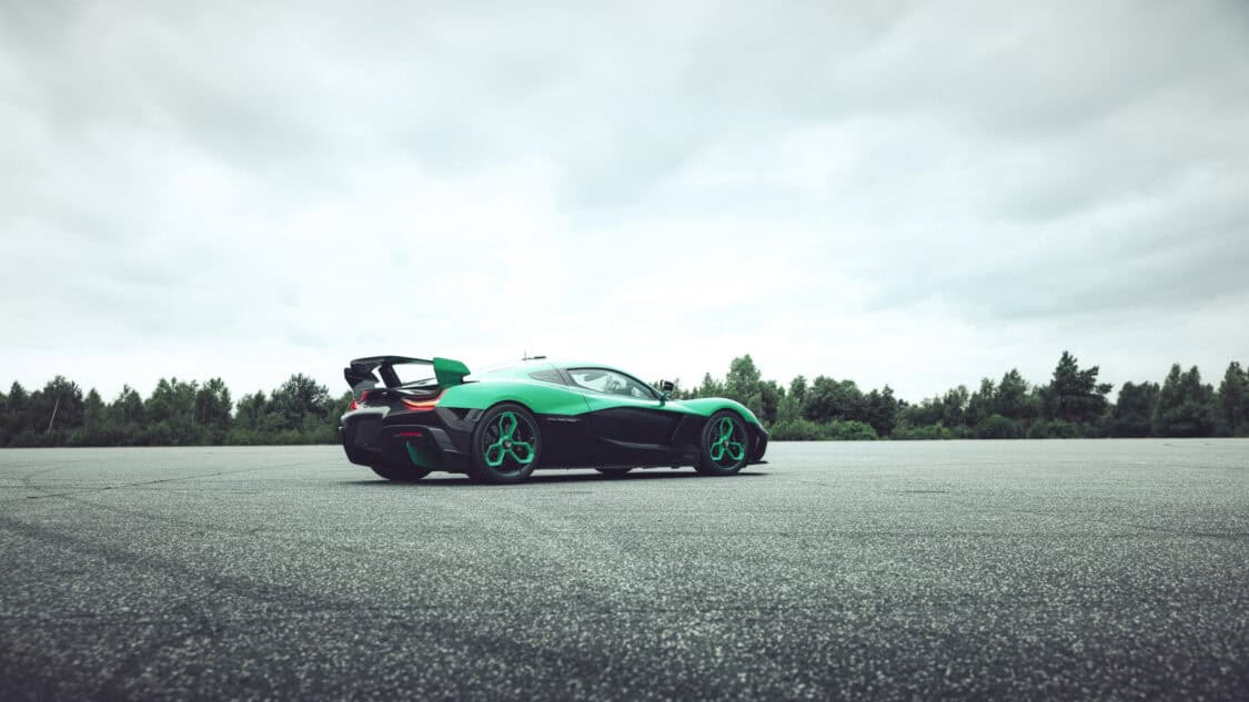 Rear three-quarter view of the Rimac Nevera R parked on a test track, highlighting its track-ready stance and exclusive green-black livery.