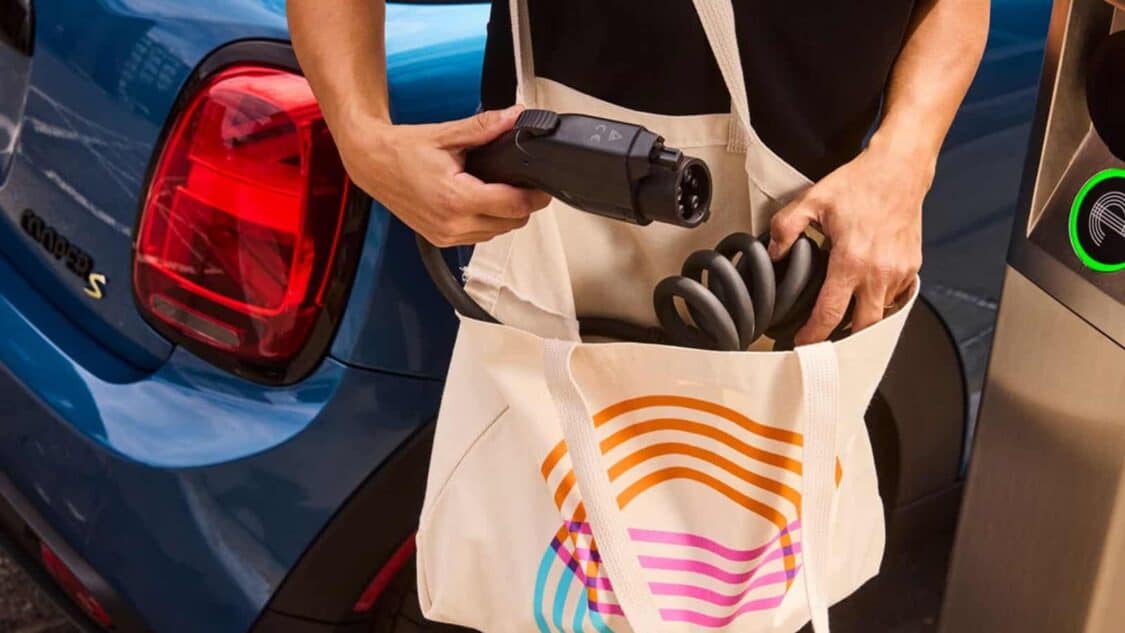 A driver retrieves an EV charging cable from a tote bag while preparing to use an it’s electric curbside charger in Alameda.