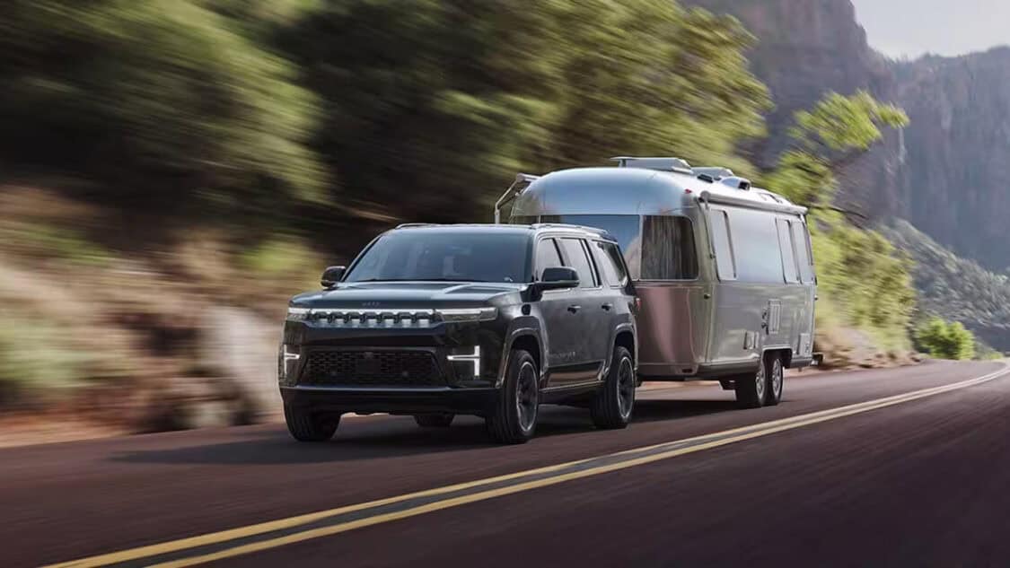 2026 Jeep Grand Wagoneer REEV towing an Airstream trailer through mountain roads.