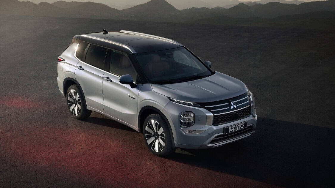 Silver Mitsubishi Outlander PHEV on an open road during sunset, highlighting electric hybrid SUV technology.