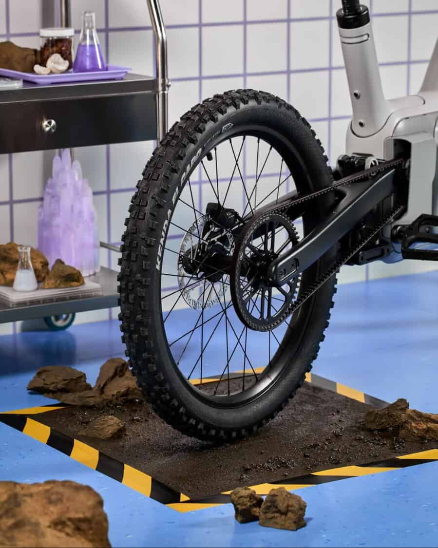 Rear wheel of the ALSO TM-B e-bike with off-road tire and belt drive positioned over rocky terrain.