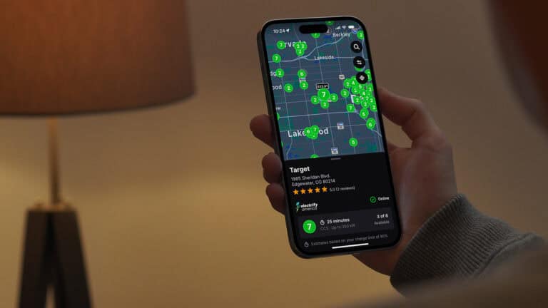 A person holding a smartphone displaying the Chargeway app with real-time EV charging prices and station locations near Lakewood, Colorado.