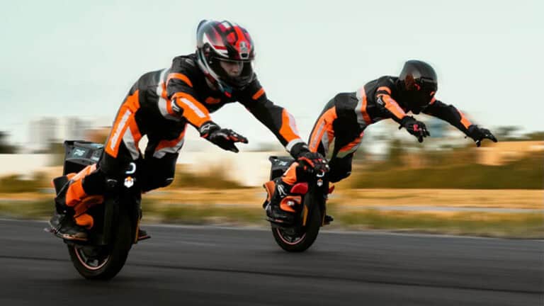 Two riders in racing gear lean forward at high speed on InMotion P6 electric unicycles, demonstrating extreme control and acceleration.