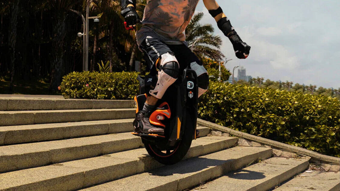 A rider wearing protective gear rides an InMotion P6 electric unicycle down concrete stairs, demonstrating balance and off-road capability.