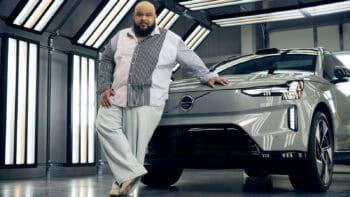 Designer Sergio Hudson leans on the fully electric Volvo EX90 inside the Charleston plant, highlighting their fashion and automotive collaboration.