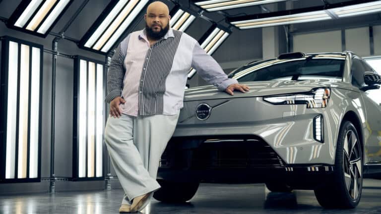 Designer Sergio Hudson leans on the fully electric Volvo EX90 inside the Charleston plant, highlighting their fashion and automotive collaboration.
