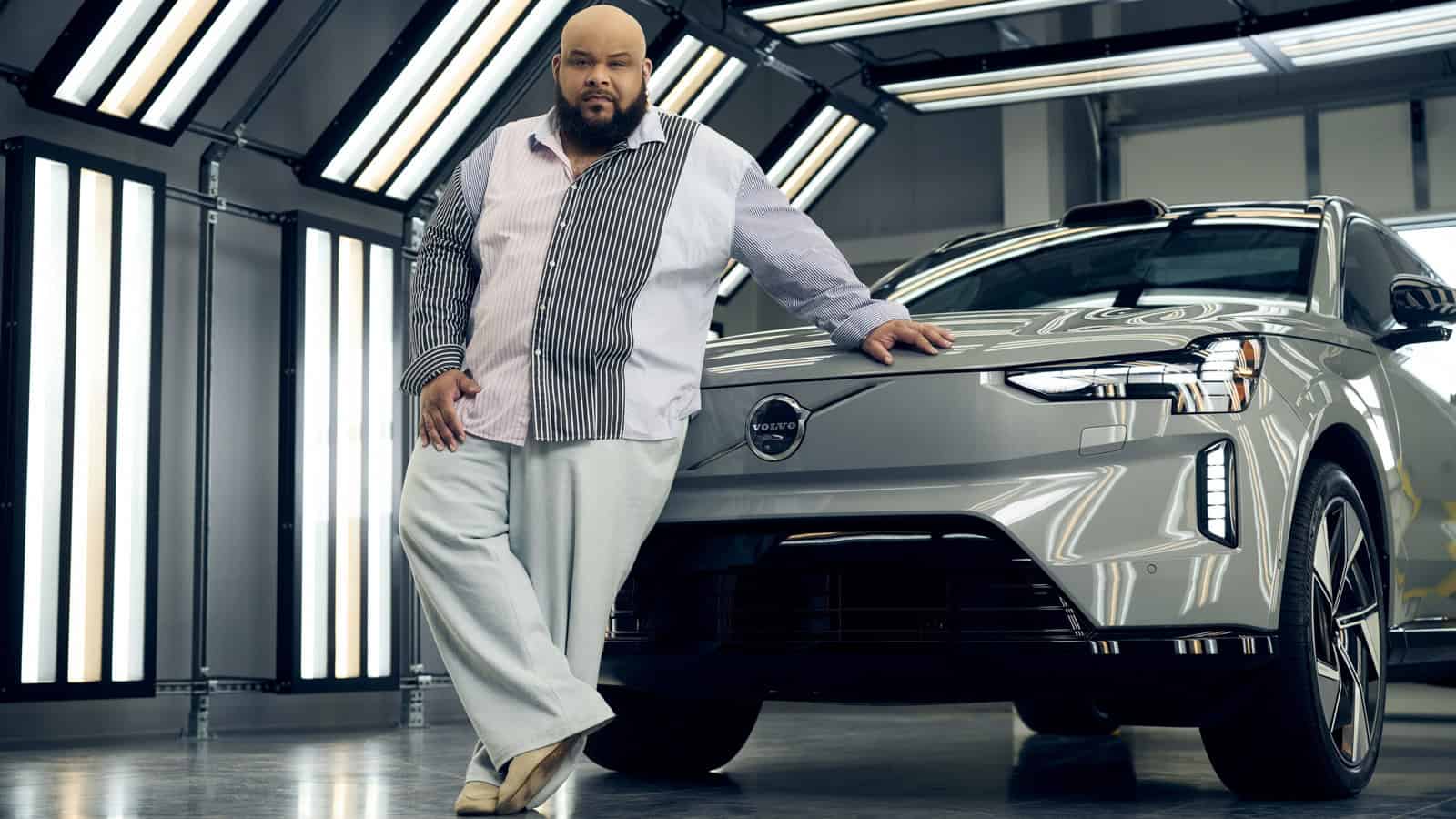 Designer Sergio Hudson leans on the fully electric Volvo EX90 inside the Charleston plant, highlighting their fashion and automotive collaboration.