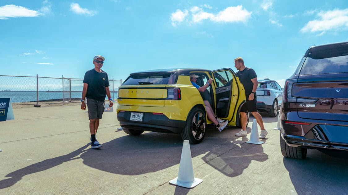 A yellow Volvo EX30 electric SUV prepares for a test drive at Electrify Expo, as attendees interact with event staff near the waterfront course.