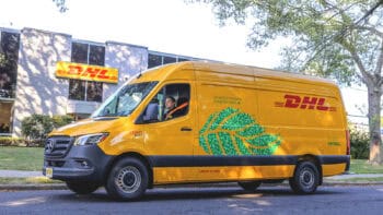 A yellow DHL Mercedes-Benz eSprinter electric van parked outside a DHL facility, highlighting its zero-emission delivery message and green leaf graphic.