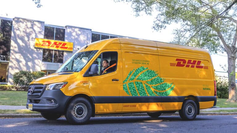 A yellow DHL Mercedes-Benz eSprinter electric van parked outside a DHL facility, highlighting its zero-emission delivery message and green leaf graphic.