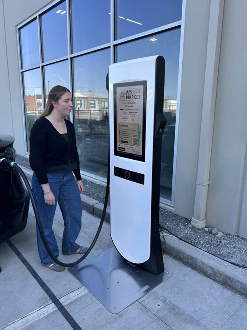 A woman charges her electric vehicle at an Electric Era RetailEdge kiosk featuring a touchscreen display and built-in HaloAI system.