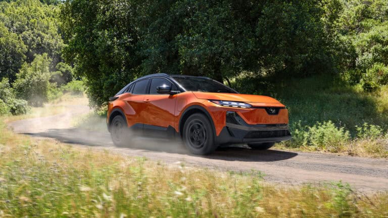2026 Subaru Uncharted Sport in Habanero Orange driving on a dirt road, highlighting its AWD capability and electric power.
