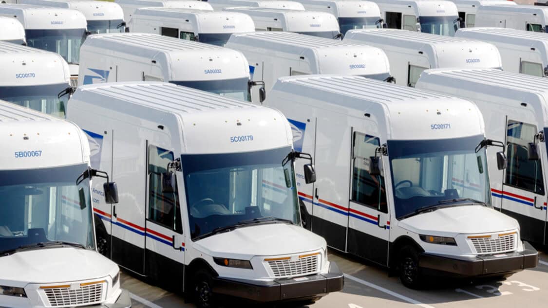 USPS electric delivery vans lined up in a fleet lot, highlighting the growth of the zero emission program.