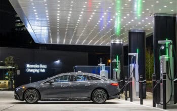 Mercedes-Benz high power EV hub with multiple power stalls under a covered canopy, featuring an electric sedan parked at a retail-style location during a short stop.
