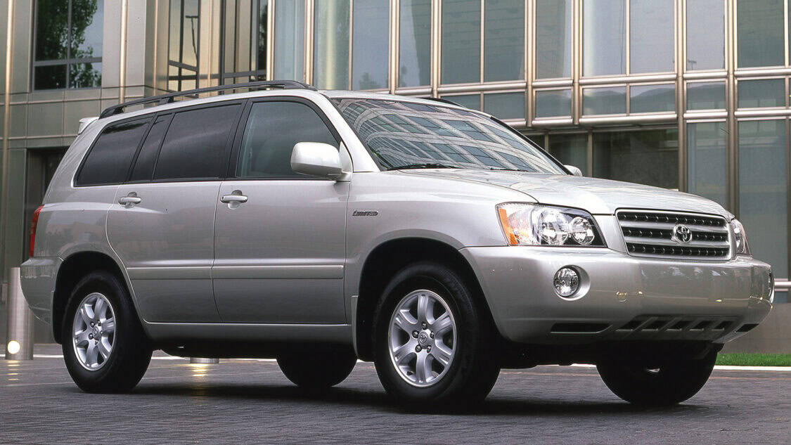 Silver 2001 Toyota Highlander SUV parked outside a modern glass office building, front three quarter view with roof rails and alloy wheels.