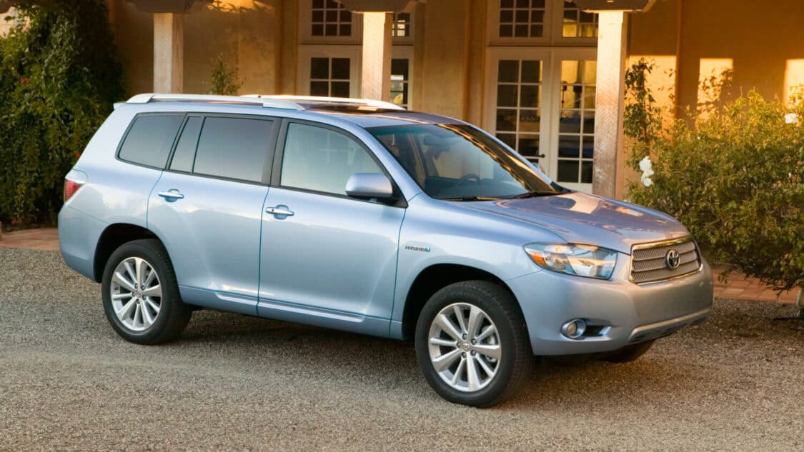 Light blue 2009 Toyota Highlander Hybrid SUV parked on a gravel driveway in front of a residential home, side front view with alloy wheels and roof rails.