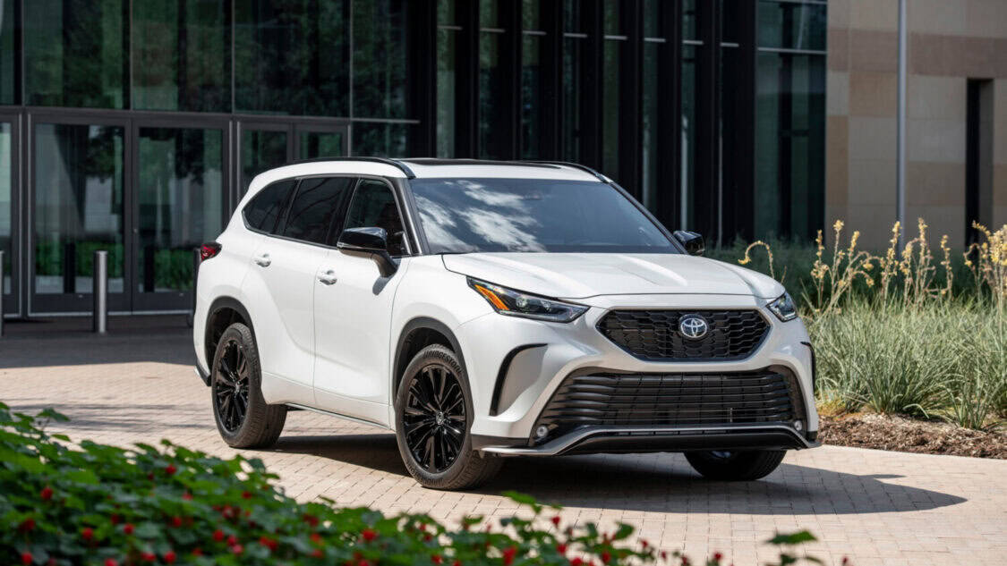 White 2005 Toyota Highlander SUV parked outside a modern office building, front three quarter view with black wheels and tinted windows.