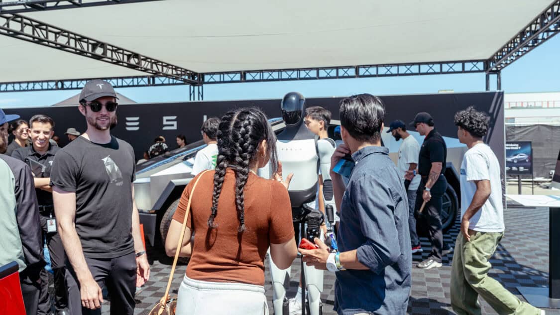 Attendees interacting with Tesla Optimus humanoid robot at Electrify Expo, reflecting Tesla’s focus on AI, robotics, and autonomy.
